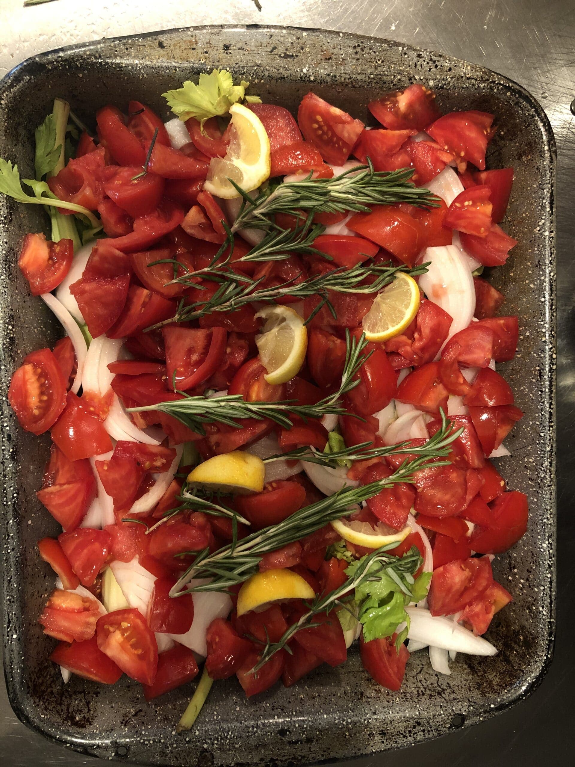 A dish of diced tomatoes, lemon slices, onion, and fresh rosemary.