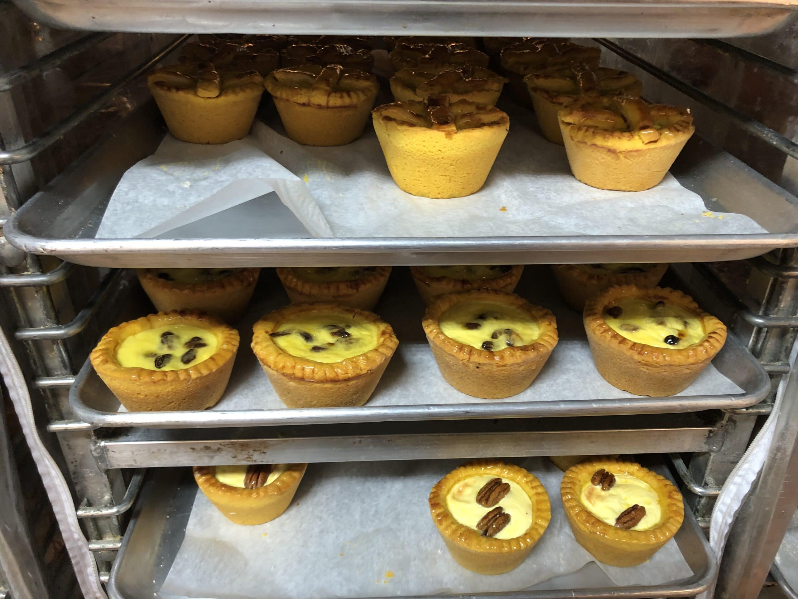 A variety of baked custard cups with nuts, arranged on metal baking trays.